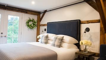 Un dormitorio con una cama grande, un cabecero de madera, una mesita de noche con lámpara y una ventana con vistas a zonas verdes.