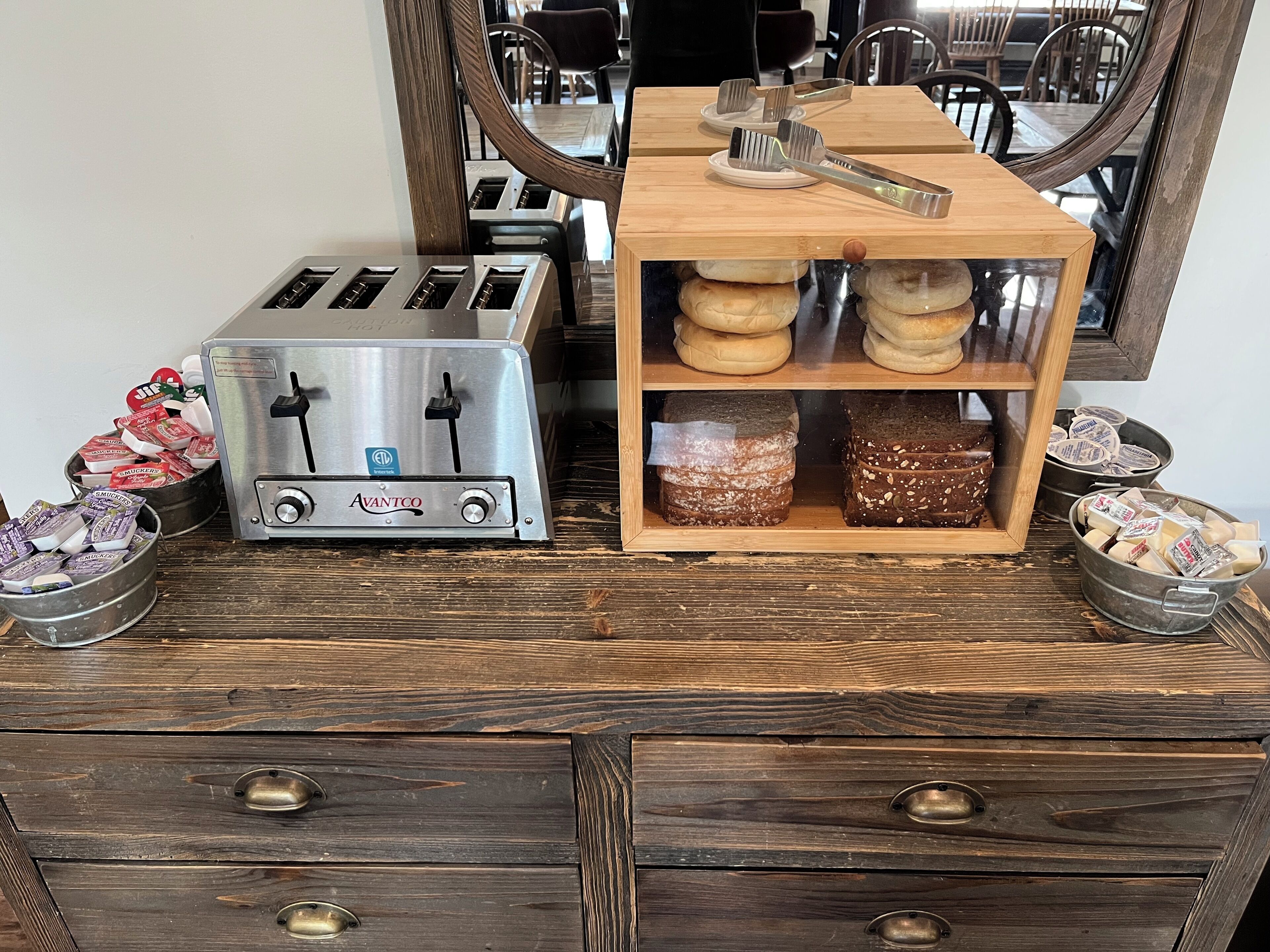 Una kitchenette con un tostador, una caja de pan de madera y un bol de aperitivos de metal.