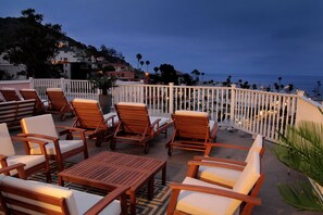 A terrace with wooden furniture, a white railing, and a view of the sea and buildings in the background. - Hotel St. Lauren (Avalon)