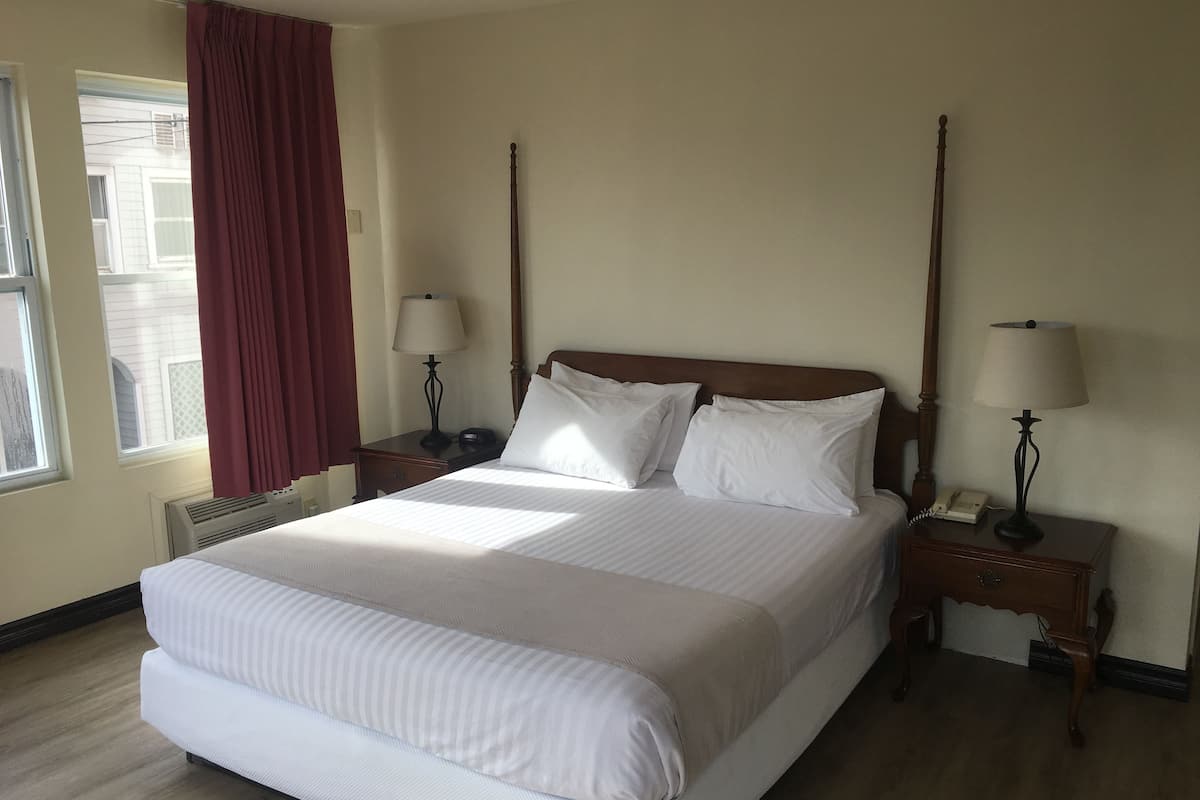 Una cama bien hecha con ropa blanca, dos mesitas de noche con lámparas y una ventana con cortinas.
