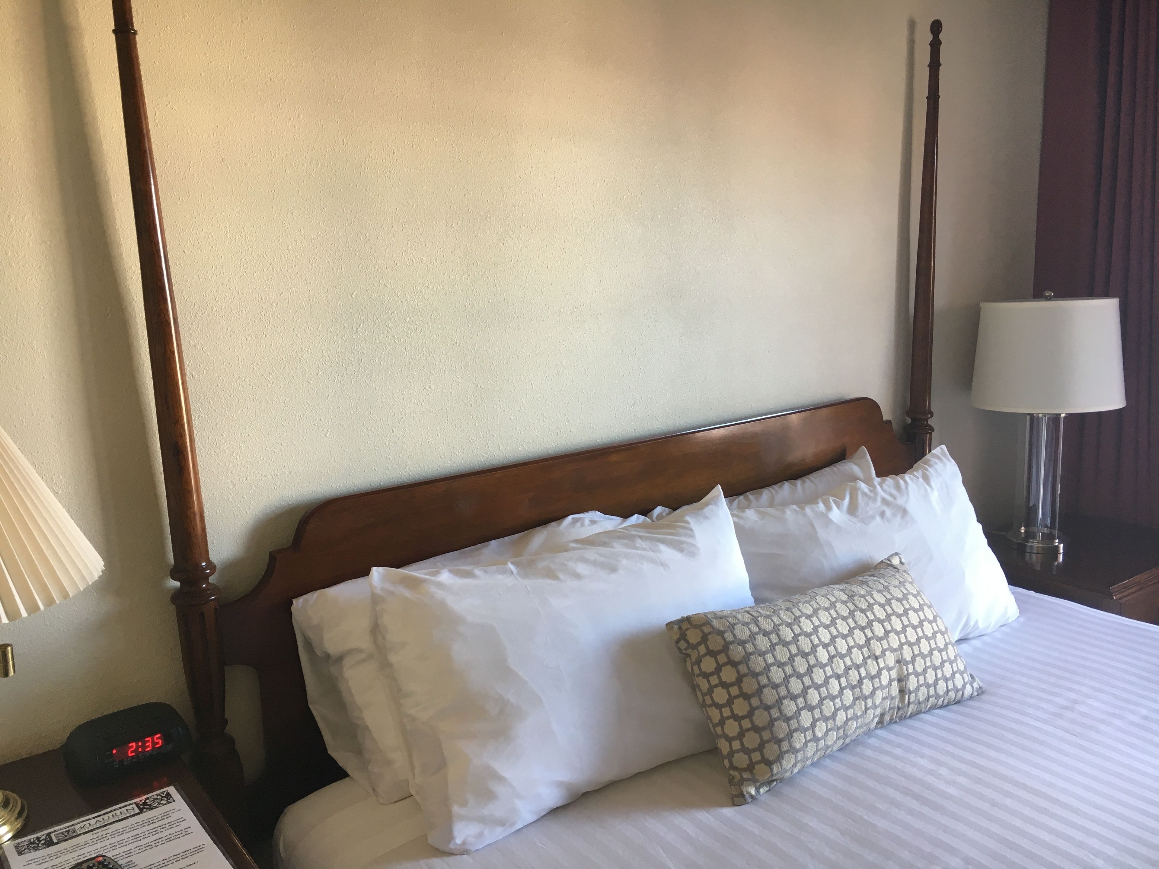 Una habitación de hotel con cabecera de madera, ropa de cama blanca y almohada estampada.
