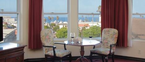 A room with a view of the ocean, a table with two chairs, and a dresser.