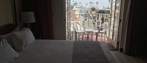 A hotel room with a bed, a nightstand, a lamp, and a view of a balcony with chairs and a table.