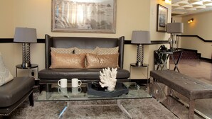 A modern hotel lobby with a leather sofa, a glass coffee table with decorative items, and a large framed picture on the wall. - Hotel St. Lauren (Avalon)