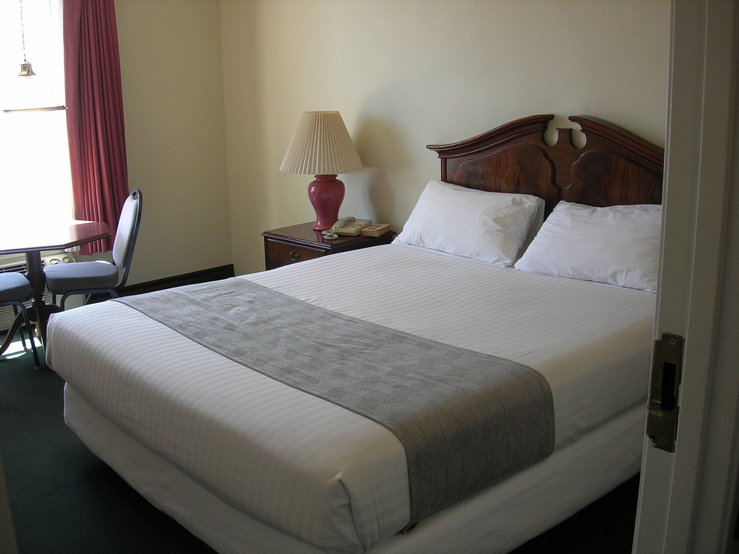 A neatly made bed with white linens, a wooden headboard, and a bedside table with a lamp and a telephone.