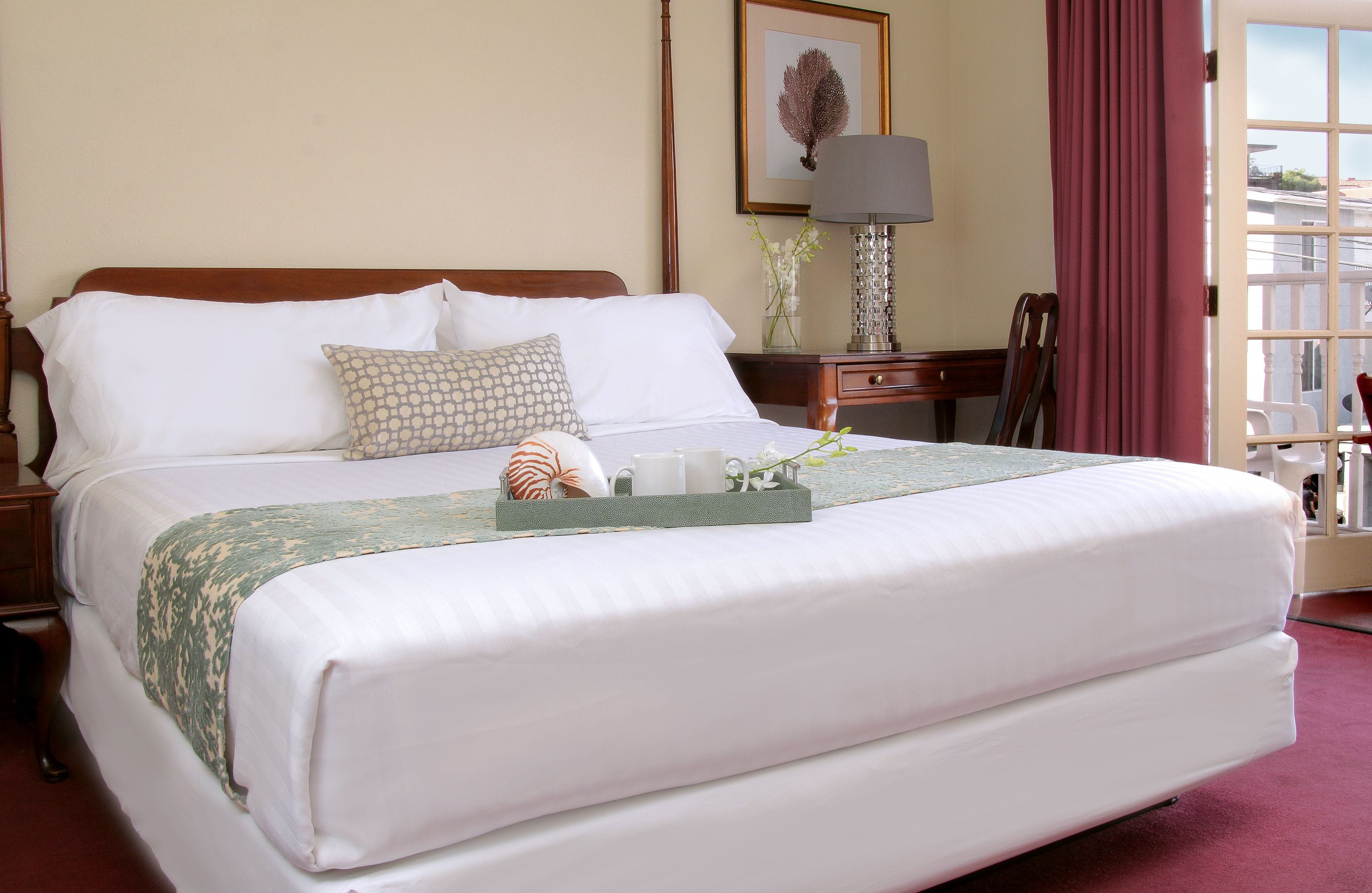 A neatly made bed with white linens, a green patterned throw, and a tray with decorative items.