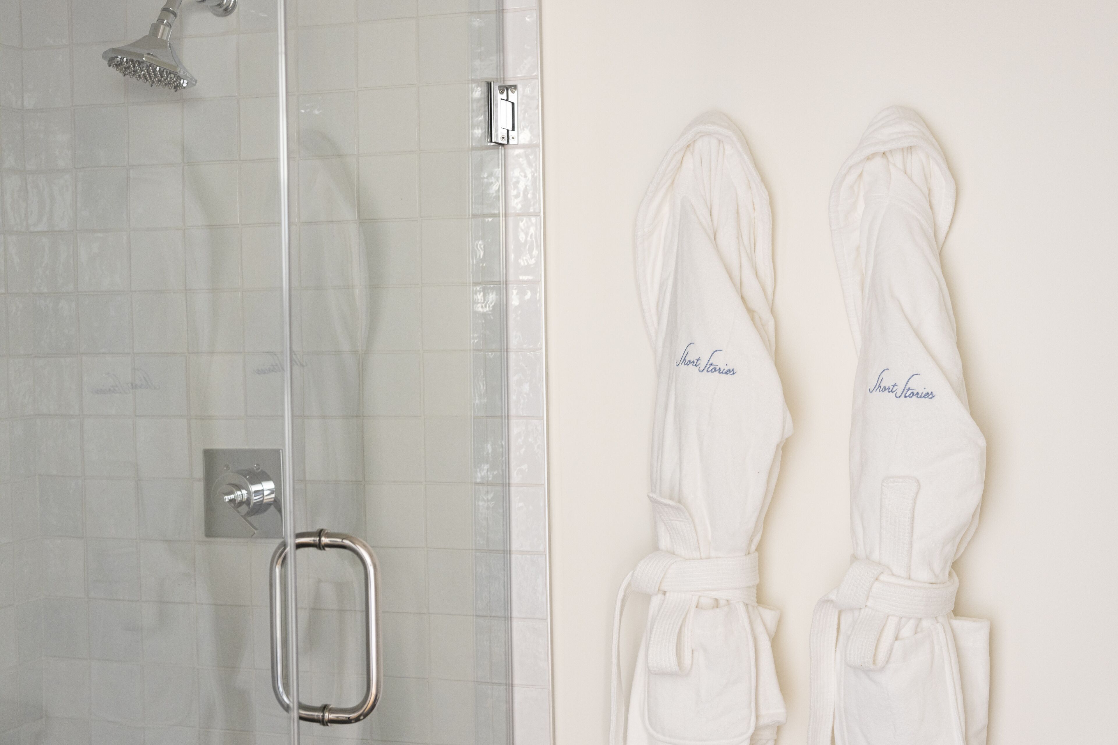 Eine Dusche mit Glastür und Metallgriff, sowie zwei weiße Bademäntel, die an einer Wand hängen.