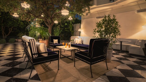 An outdoor seating area with a checkered floor, black and white striped sofas, and hanging pendant lights. - Short Stories Hotel (Los Angeles)