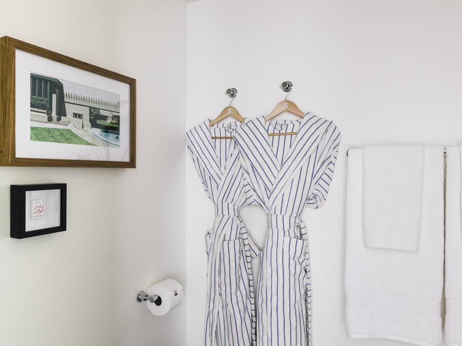 Een badkamer met een ingelijste architectuurtekening, gestreepte badjassen, een witte handdoek en een toiletrolhouder.