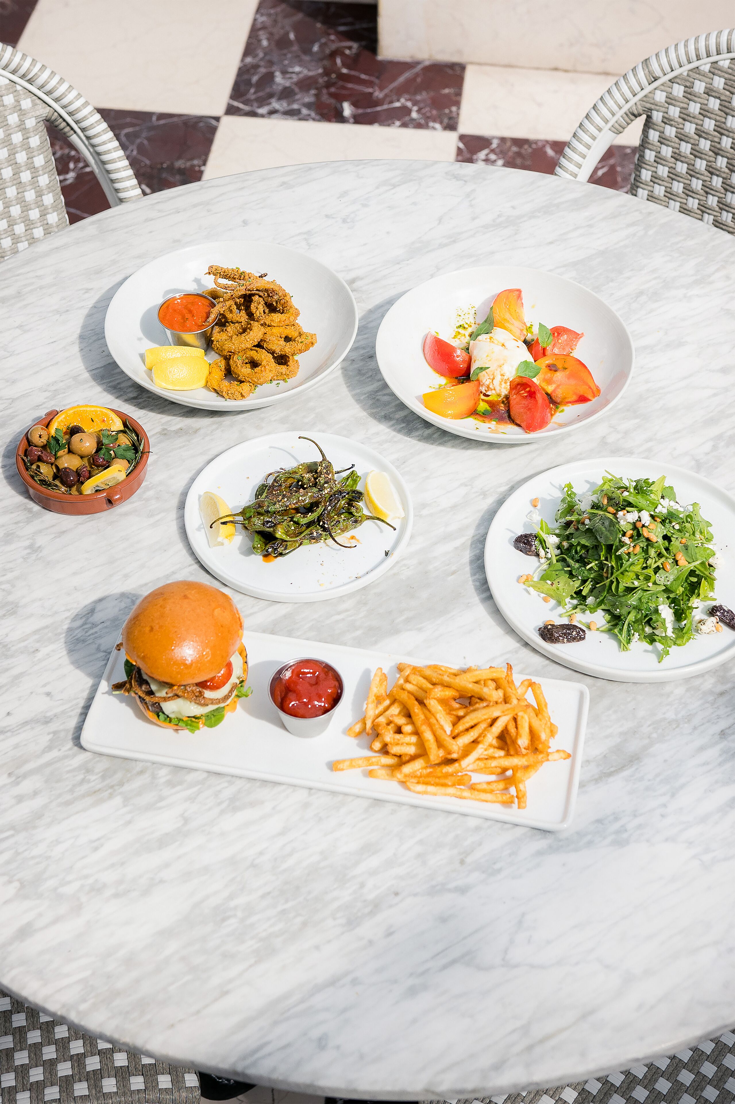 Uma mesa com diversos pratos, incluindo comidas fritas, uma salada, um hambúrguer e batatas fritas.
