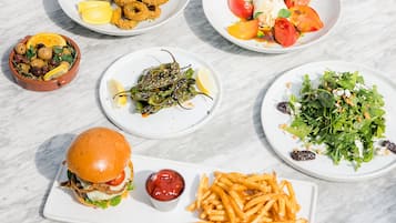 Uma mesa com diversos pratos, incluindo comidas fritas, uma salada, um hambúrguer e batatas fritas.