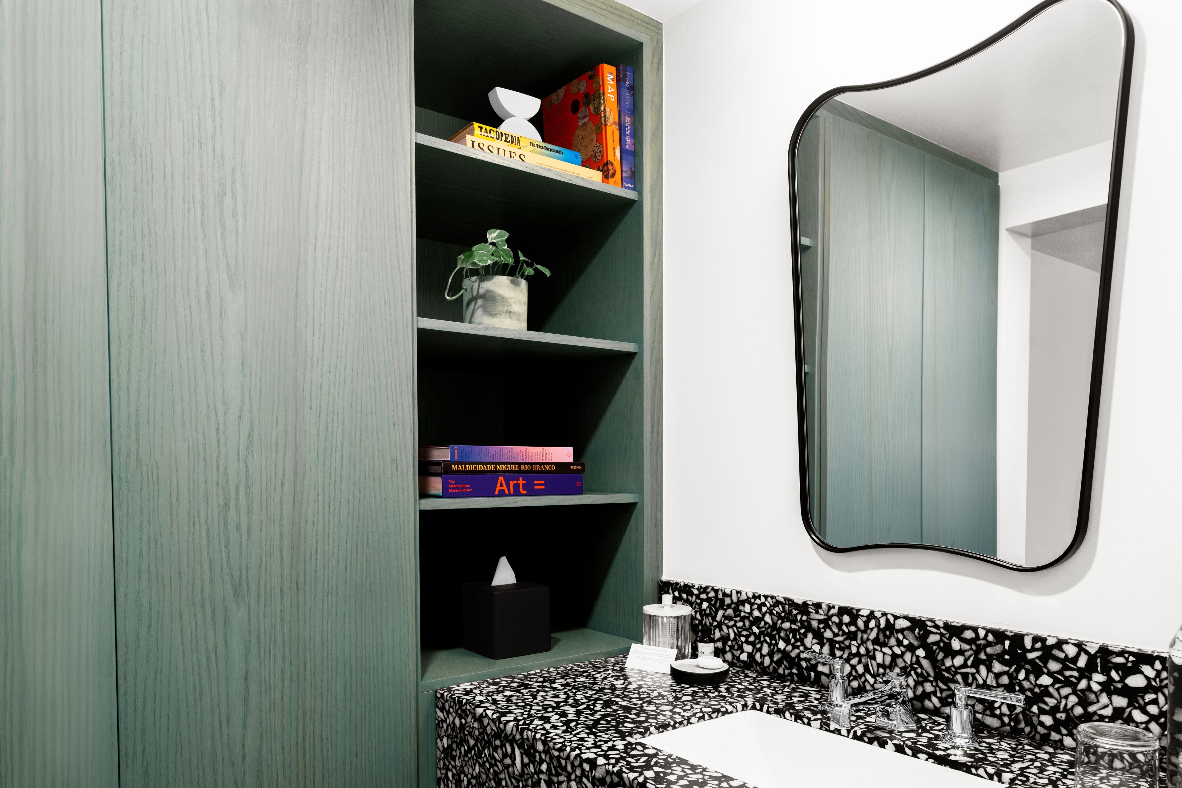 A bathroom with a green vanity, a black and white patterned sink, and shelves with books and a tissue box.