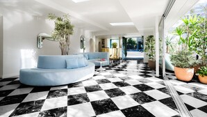 A modern living room with a checkered floor, a blue sofa, and potted plants. - Short Stories Hotel (Los Angeles)