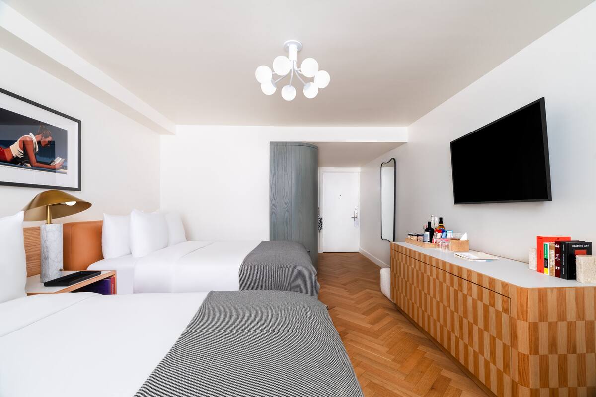A modern hotel room with a large bed, a desk, a flat-screen TV, and a wooden dresser.