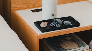 Une table de chevet en bois, sur laquelle se trouvent une lampe à abat-jour en marbre blanc, un plateau avec des lunettes de soleil et des livres.