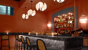A bar area with a marble countertop, black bar stools, and a well-stocked shelf of liquor bottles. - Short Stories Hotel (Los Angeles)