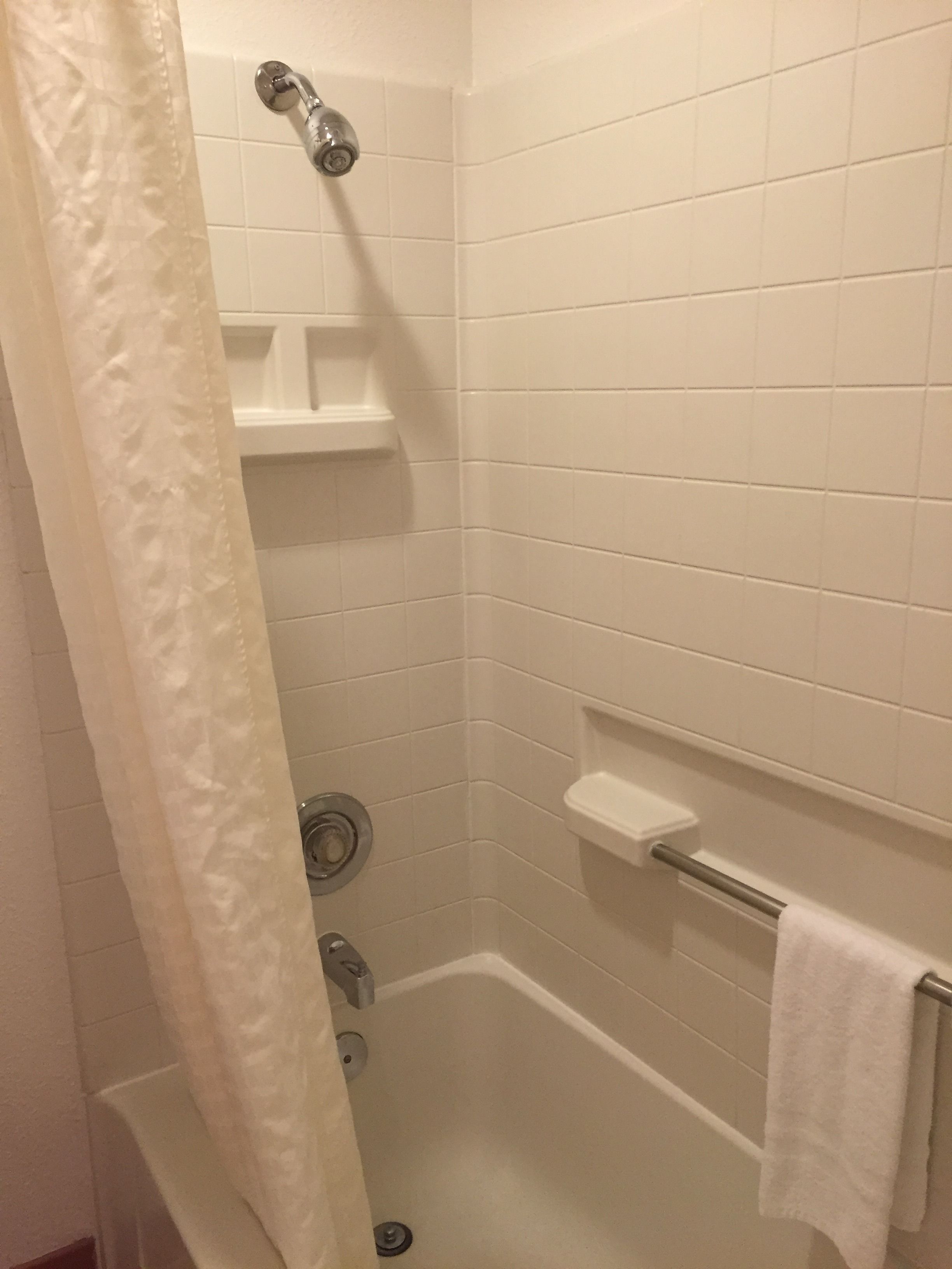 A small, white-tiled shower stall with a showerhead, a towel rack, and a shelf.