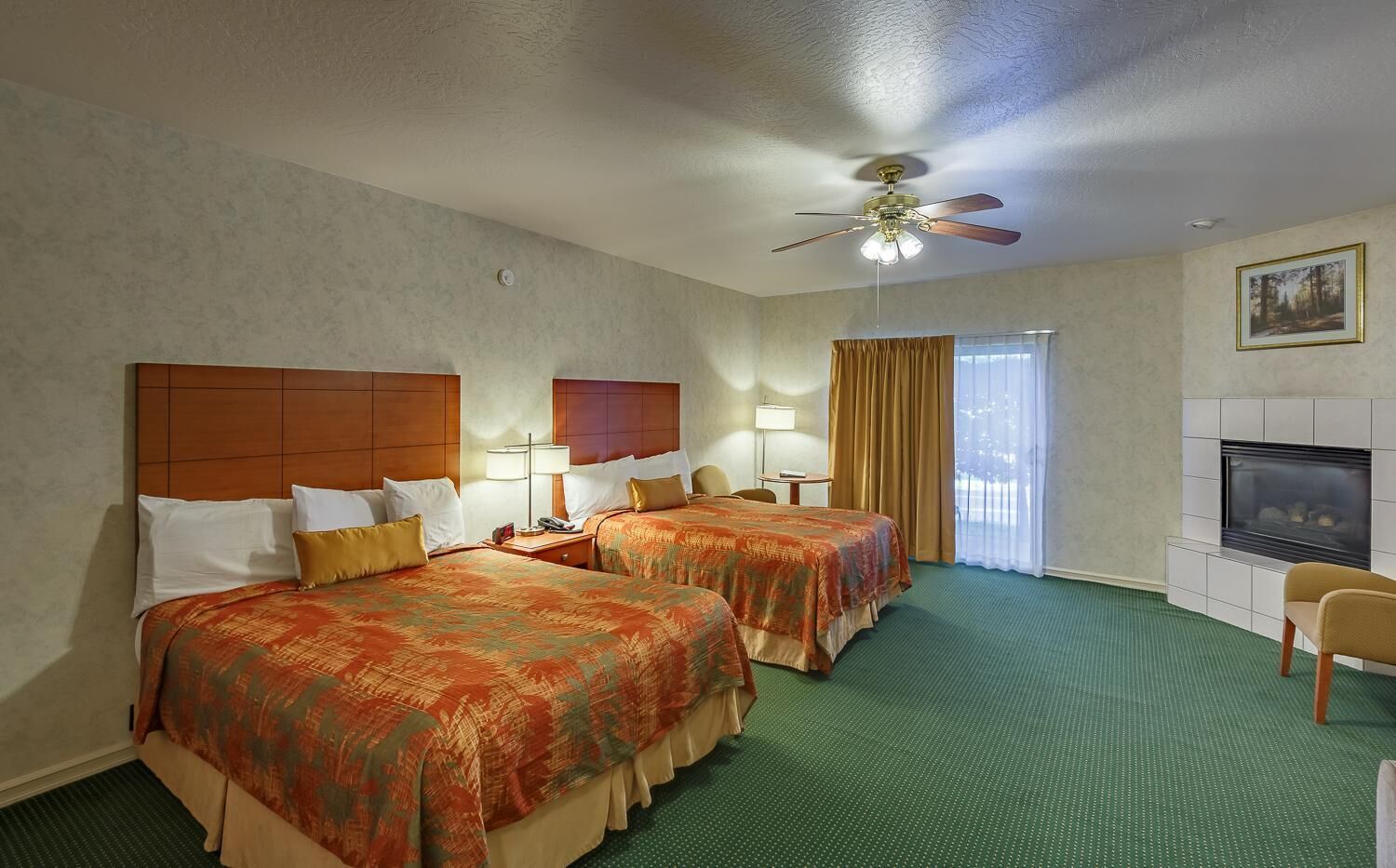 A hotel room with two beds, a ceiling fan, a fireplace, and a view of the outdoors.