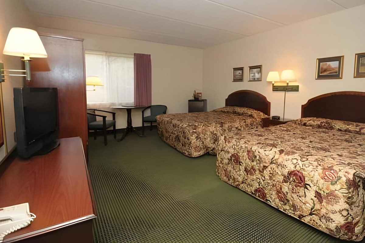 A hotel room with two beds, a desk, a television, and a chair.
