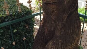 A wooden bear sculpture on a pedestal, surrounded by greenery and a metal fence.