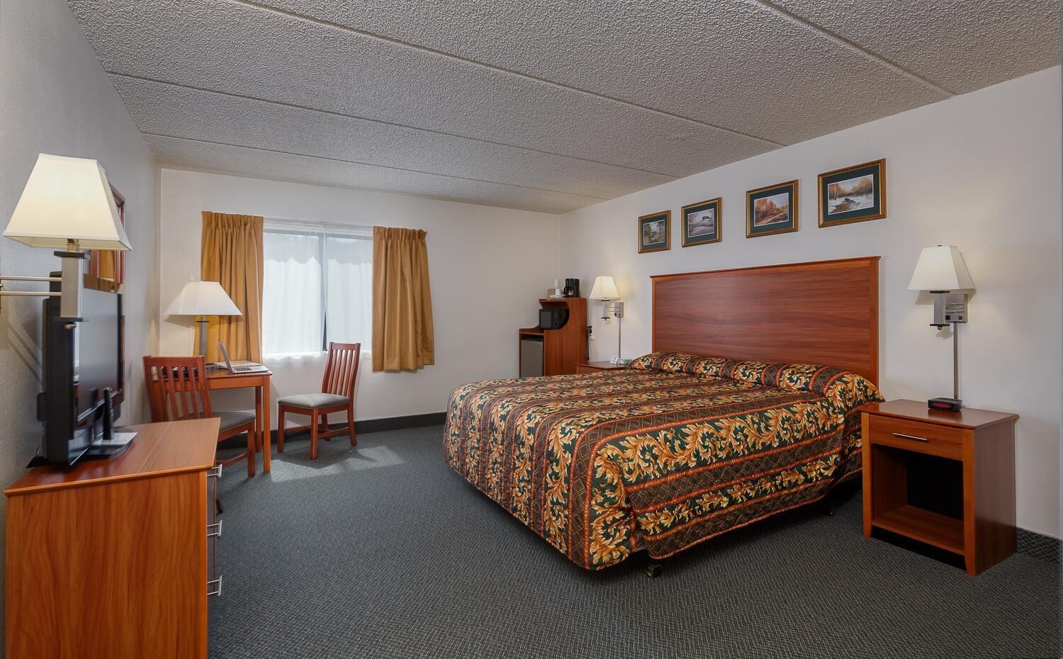A hotel room with a bed, a desk with a chair, a television, and a lamp.