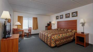 A hotel room with a bed, a desk with a chair, a television, and a lamp.