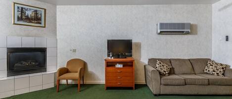 A living room with a fireplace, a television on a wooden stand, a sofa with patterned cushions, and an air conditioning unit on the wall.