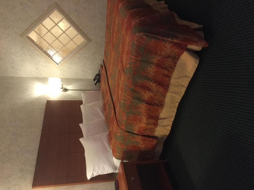 Een kamer met een bed, nachtkastje, lamp en raam.