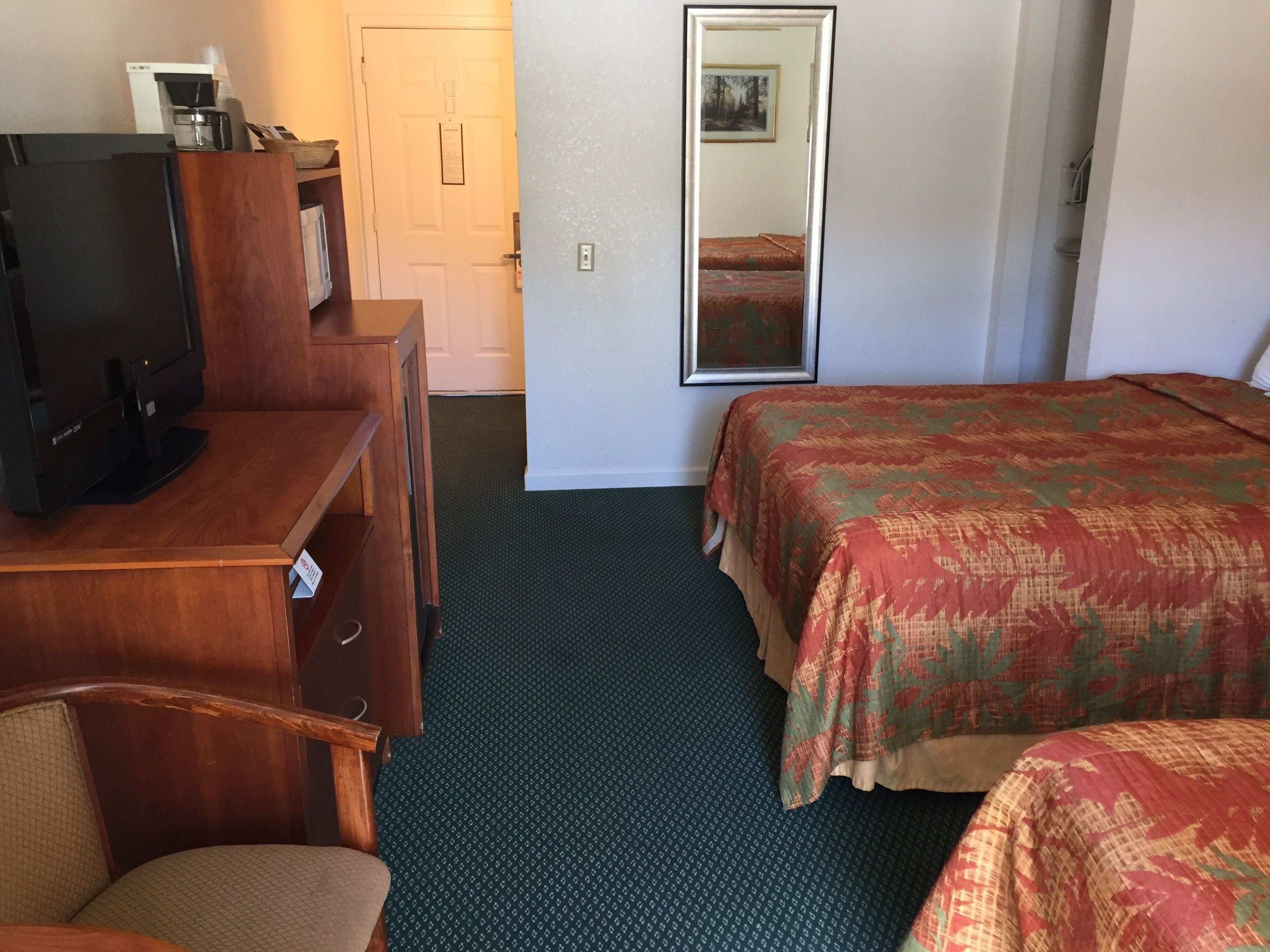 A hotel room with a desk, television, two beds, a mirror, and a door.