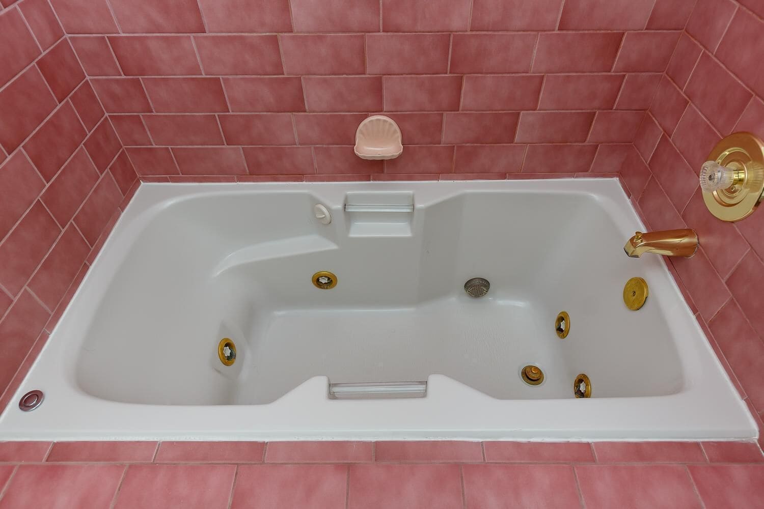 Una bañera rectangular con interior blanco, rodeada de paredes con azulejos rosas.
