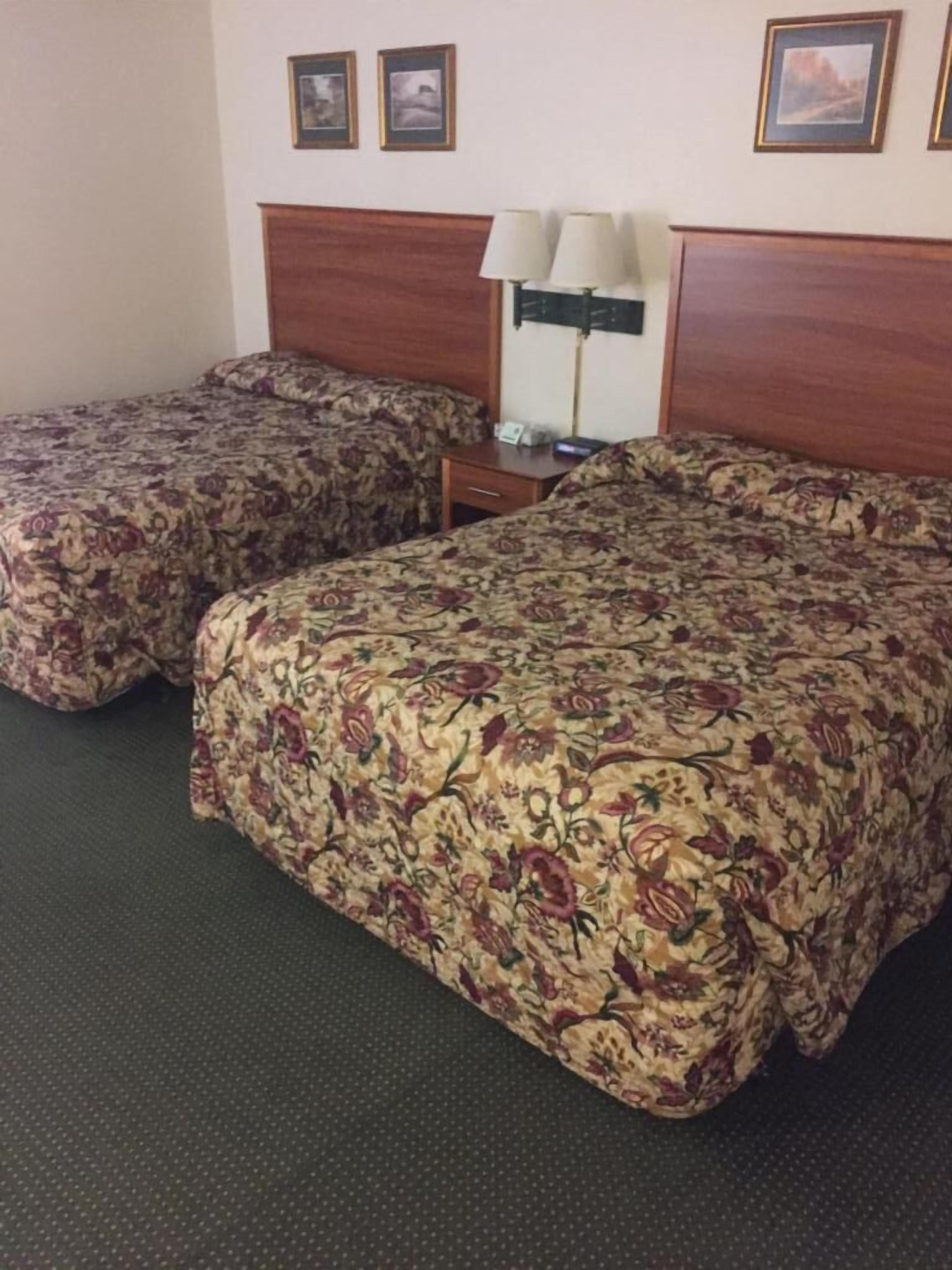 A hotel room with two single beds and a larger bed. There is a nightstand with a lamp and a small table with a phone.