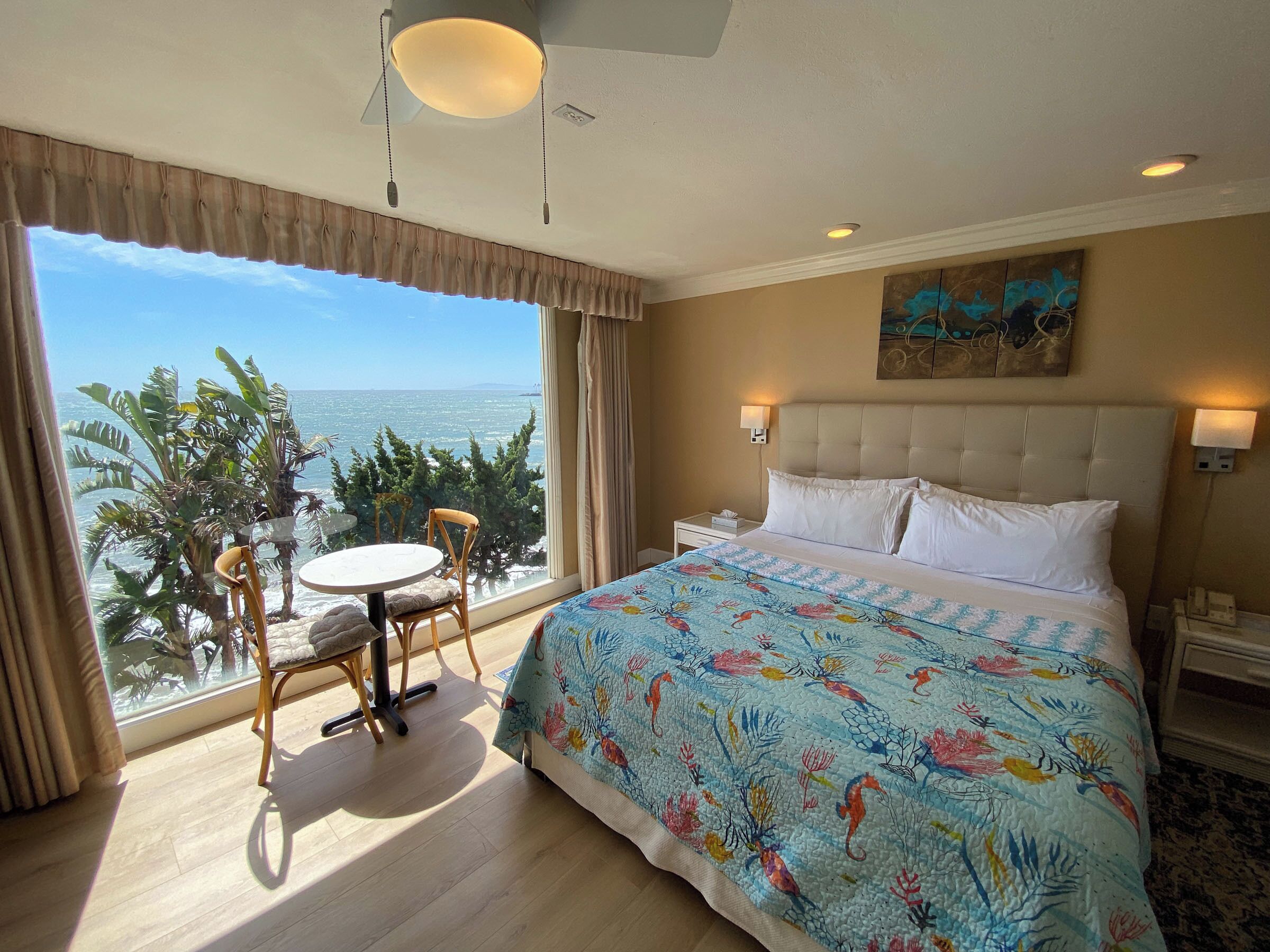 Habitación de hotel con una cama grande, una mesa redonda y una silla junto a la ventana con vistas al mar.