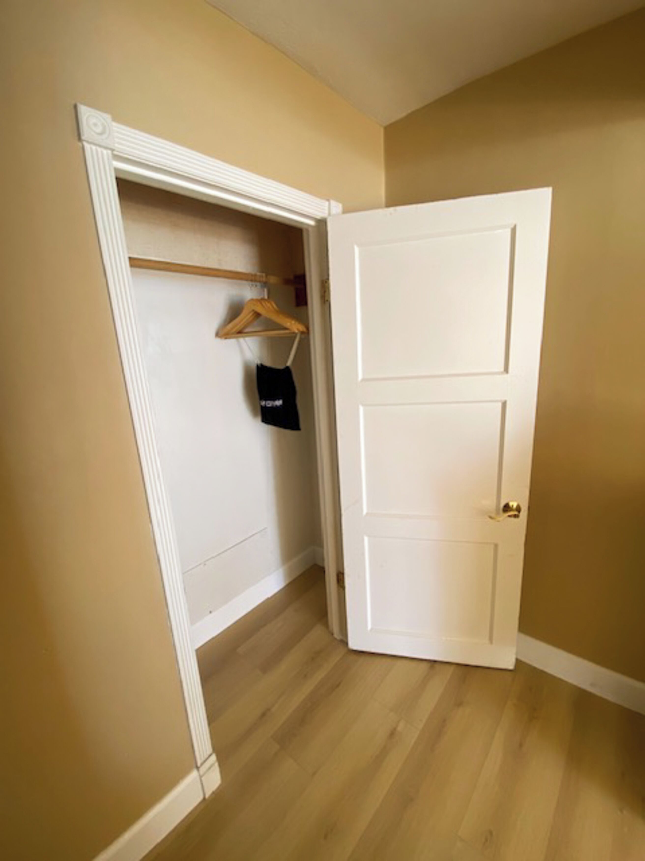 A hallway with a white door, a wooden hanger, and a black bag on a wall.