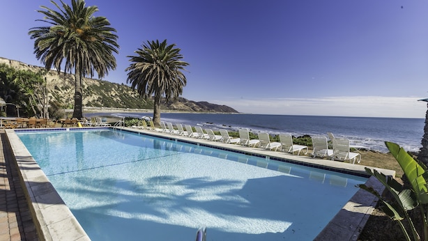 A pool with lounge chairs and palm trees, overlooking the ocean. - Cliff House Inn On The Ocean (Ventura)