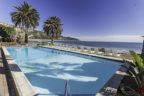 Ein Pool mit Liegestühlen und Palmen, mit Blick auf den Ozean.