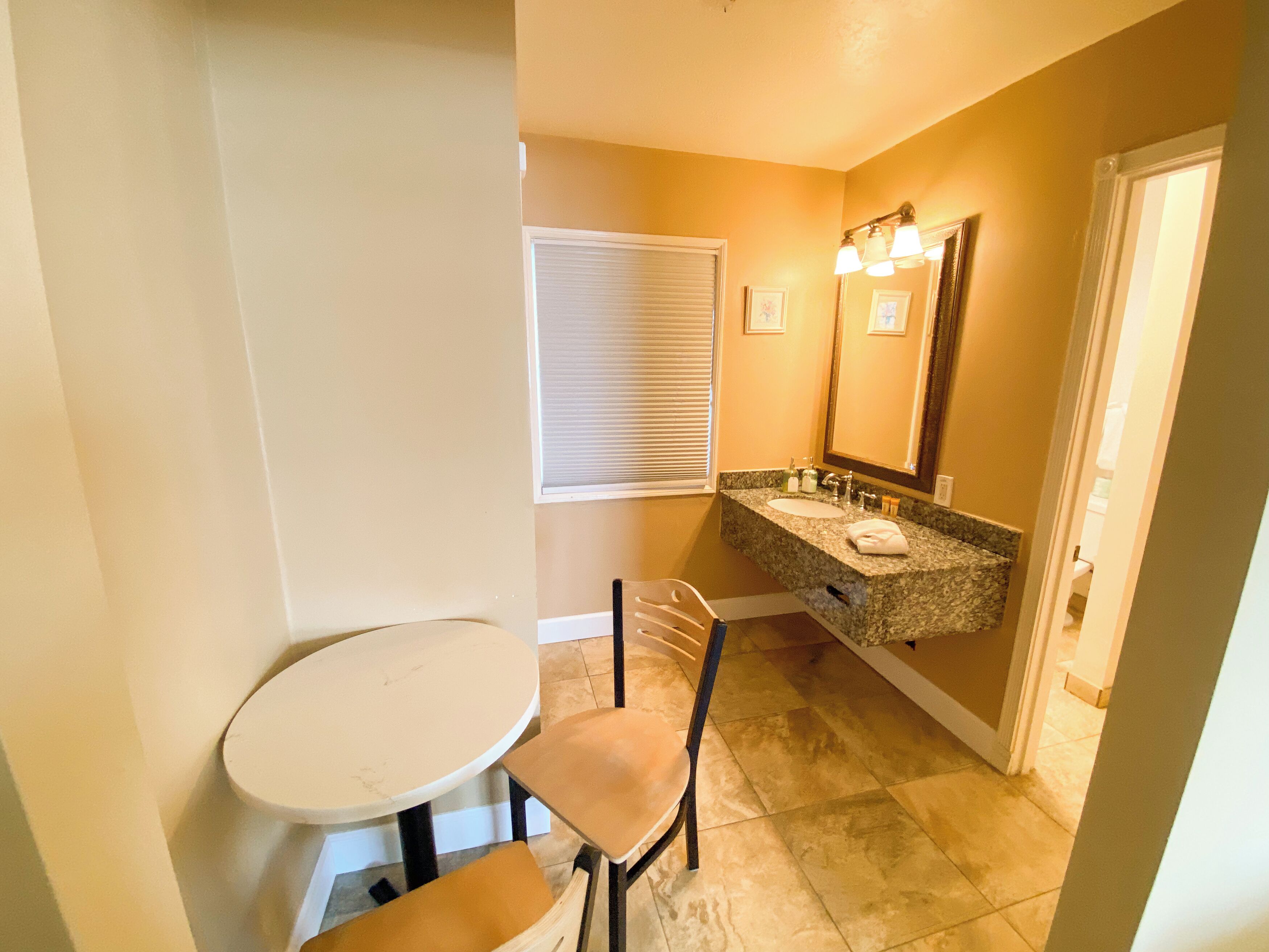 A bathroom with a sink, mirror, and a small table with a chair.