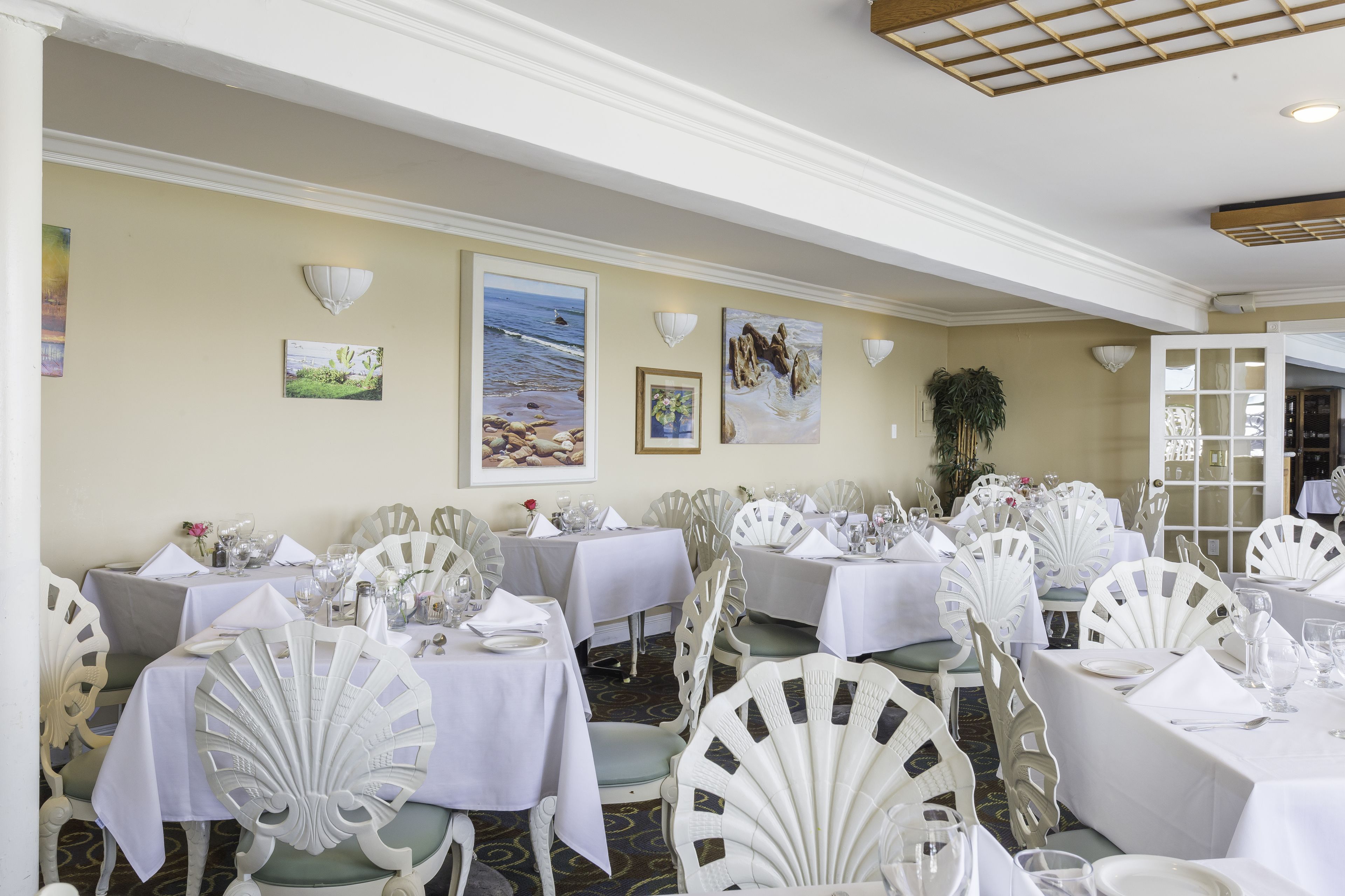 A dining area with tables set for a meal, white chairs, and framed artwork on the walls.