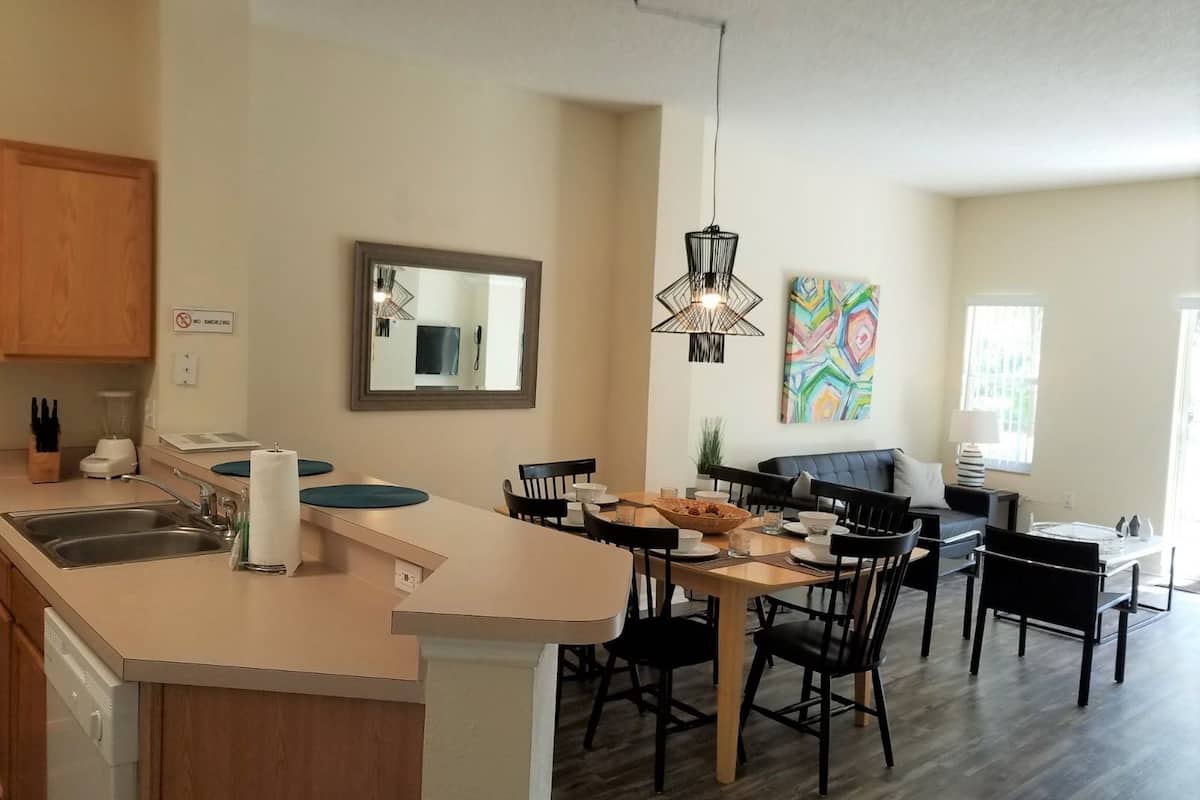 A modern kitchen with a central island, dining area with chairs, and a large mirror on the wall.