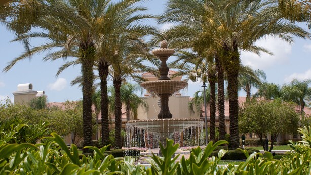 A fountain surrounded by palm trees and a building with a tiled roof.