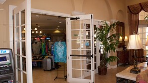 An open door leading to a retail area with various items on display, a potted plant, and a lamp on a table.