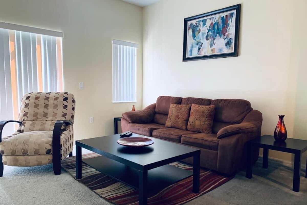 A living room with a brown sofa, a patterned armchair, a coffee table, and a framed abstract painting on the wall.