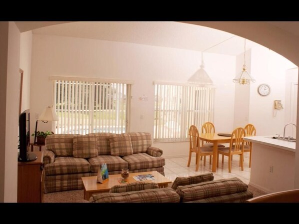 A living room with a sofa set, a dining table with chairs, and a kitchen area with a sink and a clock on the wall. - Alamo Vacation Townhomes (Orlando)