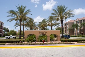 A sign for Vista Cay Resort with palm trees and a paved walkway. - Alamo Vacation Townhomes (Orlando)
