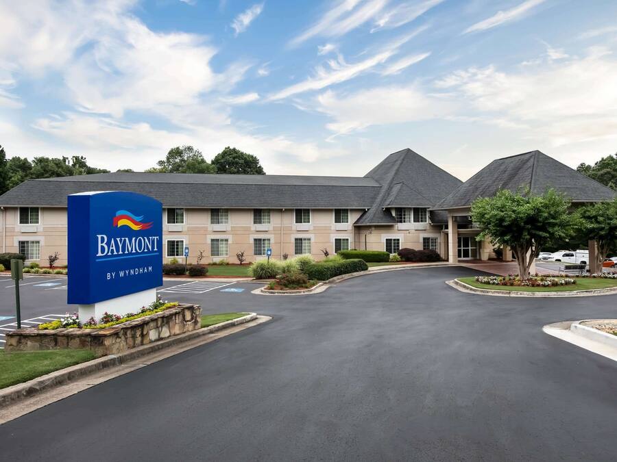 A Baymont by Wyndham hotel with a large sign, a parking lot, and a landscaped area with trees and flowers.