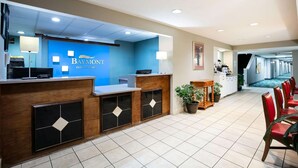 A hotel reception area with a blue wall, a reception desk, and a hallway leading to a dining area with red chairs.