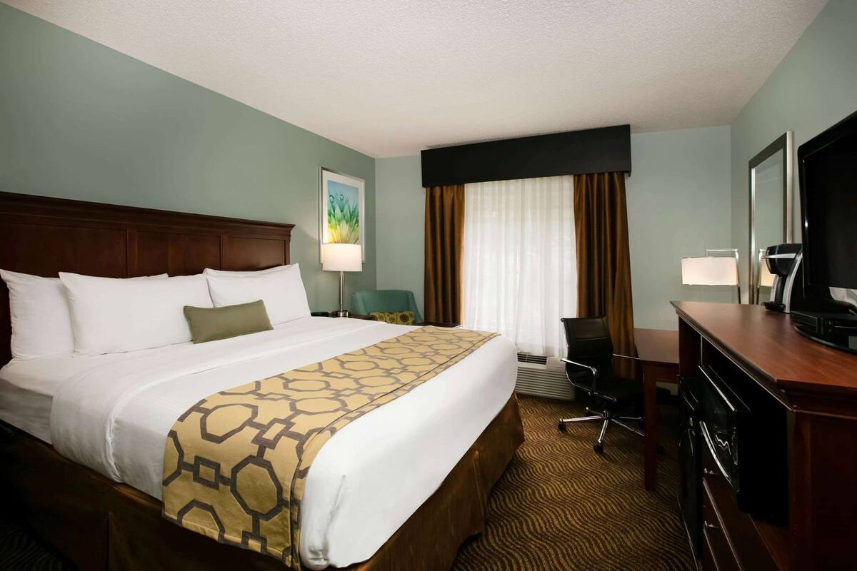 Une chambre d’hôtel avec un grand lit, un bureau avec une télévision, une chaise et une fenêtre avec des rideaux.