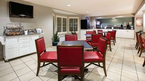 A dining area with a long table and red chairs, a buffet station, and a kitchen in the background.