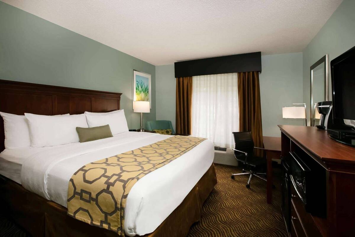Une chambre d’hôtel avec un grand lit, un bureau avec une télévision, une chaise et une fenêtre avec des rideaux.
