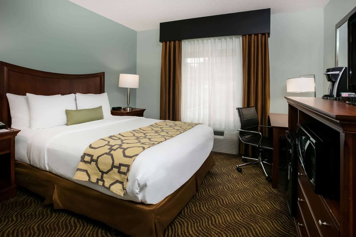 Une chambre d’hôtel avec un grand lit, un bureau, une chaise, une lampe et un téléviseur.