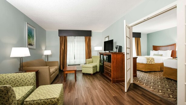 A hotel room with a sofa, armchair, small table, TV, and a bed with a patterned rug.